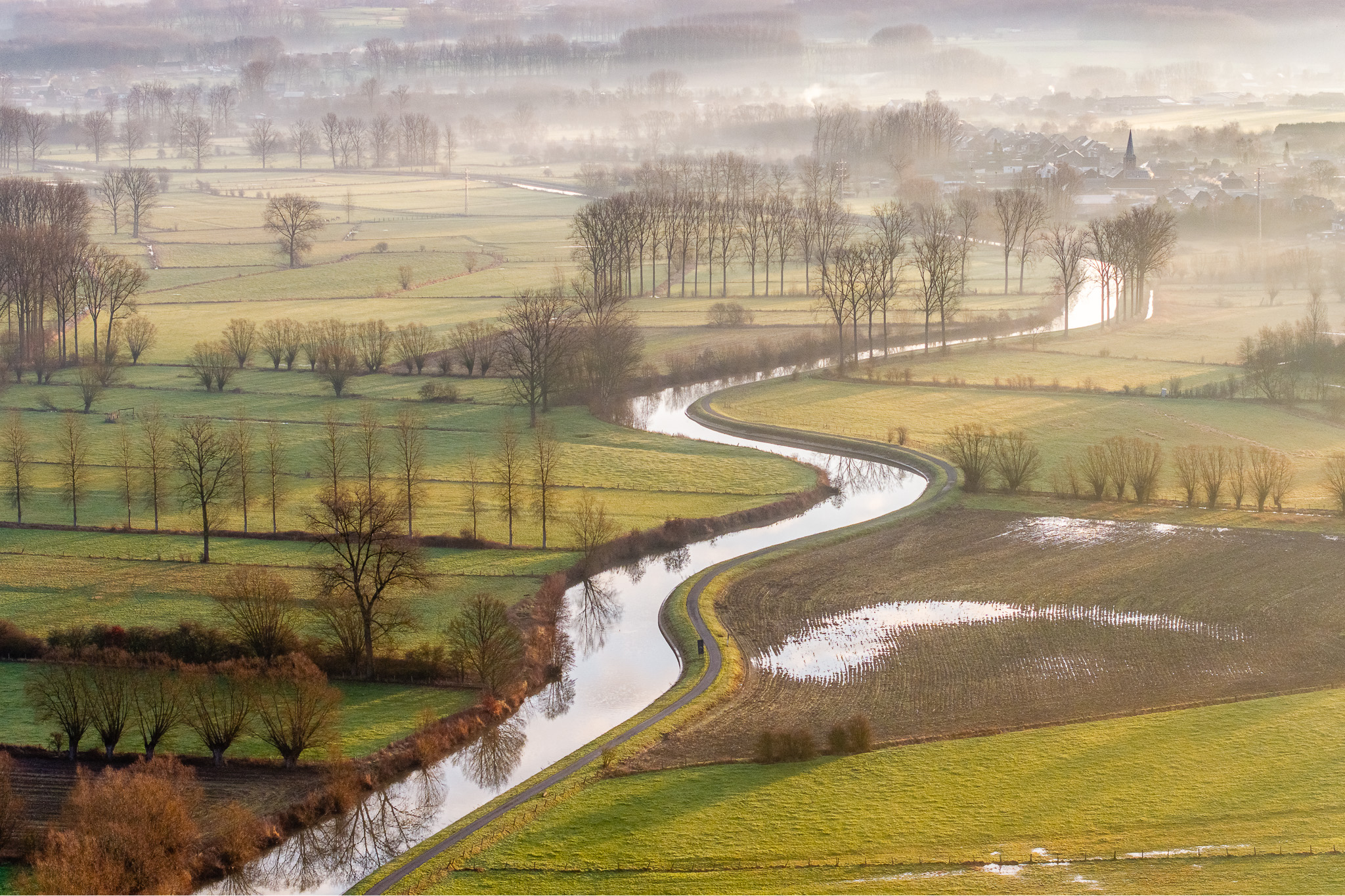 Luchtfoto van de kronkelende Dender in een mistig landschap bij Geraardsbergen tijdens zonsopkomst